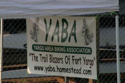 Banner for the Yargo Area Biking Association (YABA) displaying the association's logo and the slogan "The Trail Blazers Of Fort Yargo," along with the website URL. The banner is set against a chain-link fence. Fort Yargo State Park mountain bike trail.