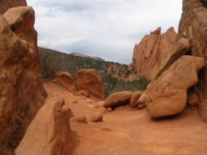 A scenic view of a rocky landscape featuring large boulders and red rock formations, with a path winding through the terrain under a cloudy sky. Garden of the Gods: Ute Trail mountain bike trail.