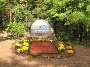 Sign for Oak Mountain State Park, surrounded by colorful flowers and greenery, indicating a left turn to enter the park. Oak Mountain State Park Bump Trail mountain bike trail.