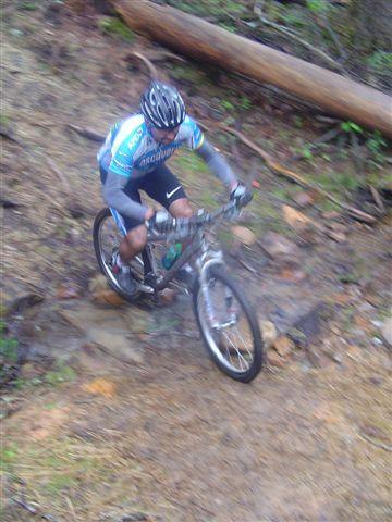 A mountain biker navigating a rocky downhill trail in a forested area, wearing a blue and gray jersey and a helmet. DuPont State Forest mountain bike trail.