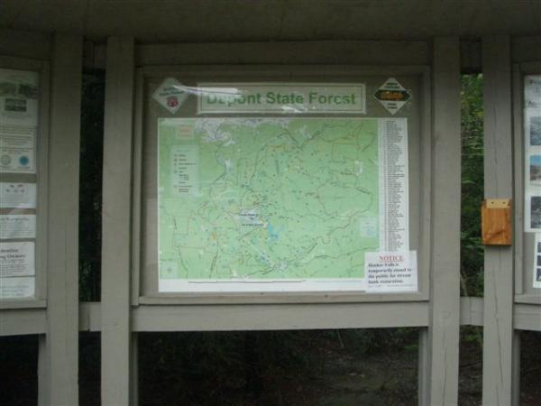 Map of Dupont State Forest displayed on a wooden information board, featuring trails, water features, and important notes for visitors. DuPont State Forest mountain bike trail.
