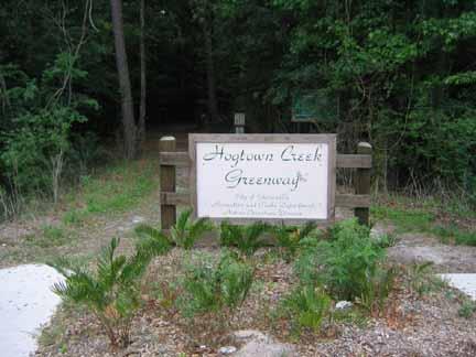Sign marking the entrance to Hogtown Creek Greenway, surrounded by lush greenery and trees. The sign features the name of the greenway and information about the park. Hogtown Creek Greenway mountain bike trail.