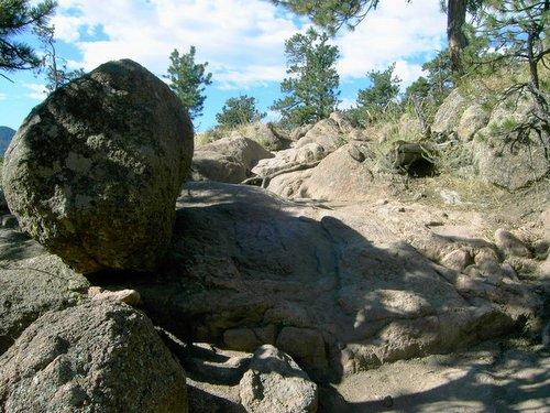Rocky terrain featuring large boulders and scattered smaller rocks, surrounded by trees and a clear blue sky. The scene captures natural formations and textures in a mountainous area. Hall Ranch mountain bike trail.