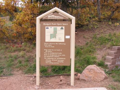 Sign for Blodgett Peak Open Space with rules and a map. The sign features guidelines for park visitors, including pet policies and prohibited activities. Surrounding area includes trees with fall foliage. Blodgett mountain bike trail.
