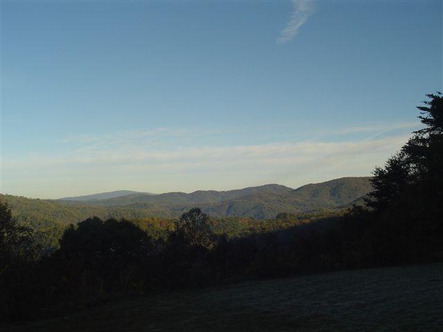 Scenic view of rolling mountains under a clear blue sky, with green trees in the foreground and soft, layered ridges extending into the distance. The landscape is tranquil and reflects a serene natural environment. Chilhowee trail system mountain bike trail.