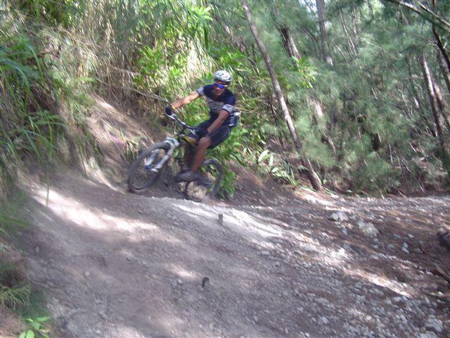 A mountain biker navigating a rocky trail in a lush forest setting, demonstrating skill as they lean into a curve. Oleta River State Park mountain bike trail.