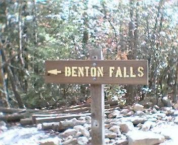 Wooden sign indicating the direction to Benton Falls, featuring an arrow pointing left, surrounded by wooded area and rocky terrain. Chilhowee trail system mountain bike trail.