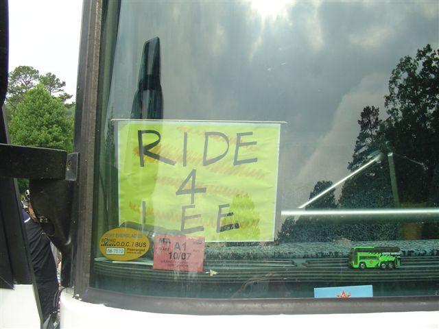 A handmade sign taped to the windshield of a bus that reads "RIDE 4 FREE" in bold letters, with a bright yellow background. The bus's interior is partially visible, and there are various stickers and a small green toy bus on the dashboard. Tsali Right Loop mountain bike trail.