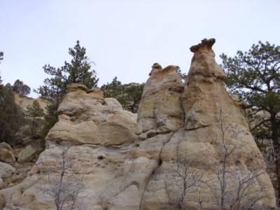 A rocky landscape featuring unique, towering rock formations surrounded by sparse trees and a cloudy sky. The formations are sculpted and uneven, resembling natural sculptures. Palmer Park mountain bike trail.