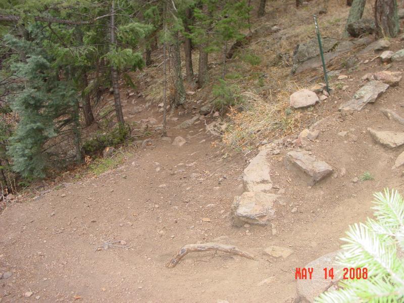 A dirt path winding through a forested area, surrounded by trees and rocky terrain. The image shows a slight incline with scattered rocks and roots along the trail. The date "May 14, 2008" is visible in the corner. Palmer Trail / Section 16 mountain bike trail.