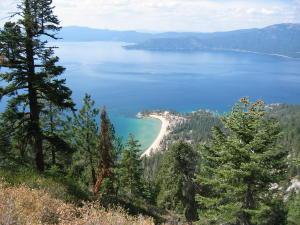 A scenic view of a tranquil lake surrounded by mountains, with a sandy beach and lush green trees in the foreground. Flume Trail mountain bike trail.