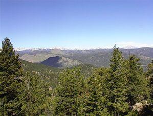 Panoramic view of a mountainous landscape featuring rolling hills, evergreen trees, and distant snow-capped peaks under a clear blue sky. Walker Ranch mountain bike trail.