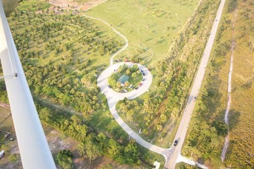 Aerial view of a circular landscaped area with a gazebo and parking lot, surrounded by green trees and grassy fields, alongside a road. Caloosahatchee Regional Park mountain bike trail.