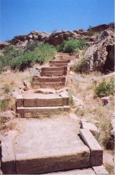 Stone steps leading up a grassy hillside with rocky outcrops under a clear blue sky. Coyote Ridge mountain bike trail.