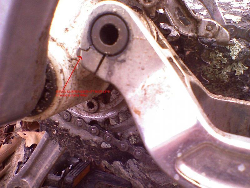 Close-up image of a bicycle's crankset showing signs of wear and dirt, with a visible crack in the rear suspension component. An arrow and text indicate the need for repair. The bicycle chain and parts of the drivetrain are also partially visible in the background. Elizabeth Furnace mountain bike trail.