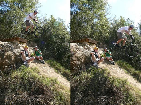 A split image showing two scenes of a mountain biker jumping off a ramp. On the left, the biker is poised to take off, while two spectators sit on the ground nearby, watching the jump. On the right, the biker is airborne, leaving the ramp and performing the jump, with the same spectators in the foreground. Both scenes are set in a lush, green outdoor environment surrounded by trees. Santos mountain bike trail.