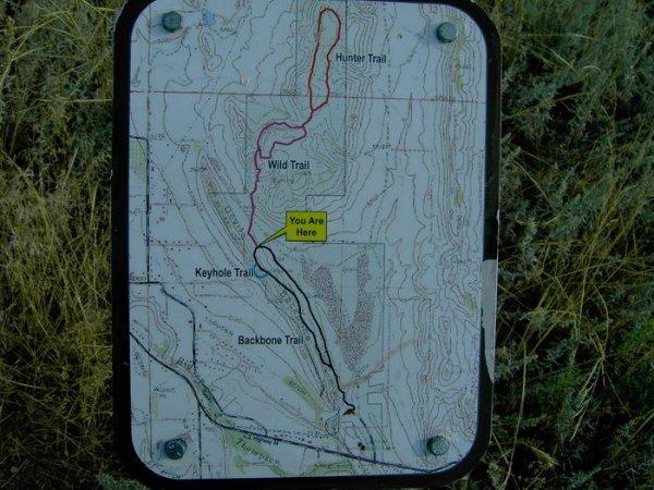 Trail map indicating various hiking paths, with labels for the Hunter Trail, Wild Trail, Keyhole Trail, and Backbone Trail. A highlighted section marked "You Are Here" shows the user's current location on the map. The background includes grass and vegetation. Devil's Backbone mountain bike trail.