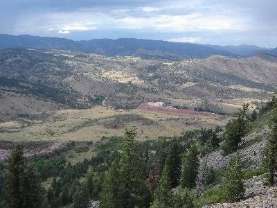 A panoramic view of a mountainous landscape with rolling hills, patches of green trees, and a valley dotted with various terrains under a cloudy sky. Heil Valley Ranch mountain bike trail.
