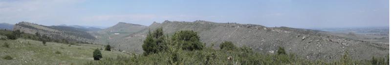 A panoramic view of rocky hills and grassy plains under a clear blue sky, showcasing the natural landscape with patches of greenery and distant mountains on the horizon. Rabbit Mountain Loop mountain bike trail.