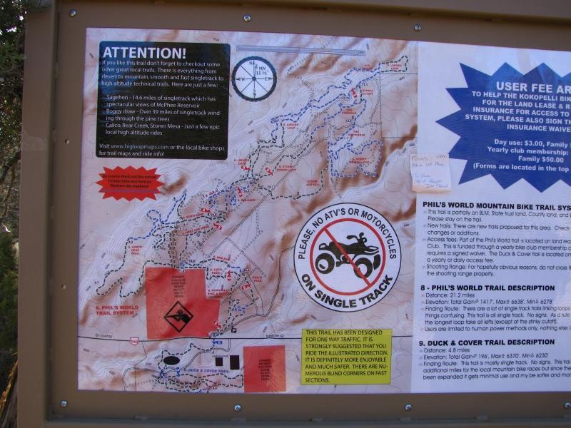 An informational sign detailing the Phil's World Mountain Bike Trail system, featuring a map with marked trails, user fee information, and rules against ATVs and motorcycles on single track. The sign provides safety and trail description guidelines, along with contact details for local bike shops. Phil's World mountain bike trail.