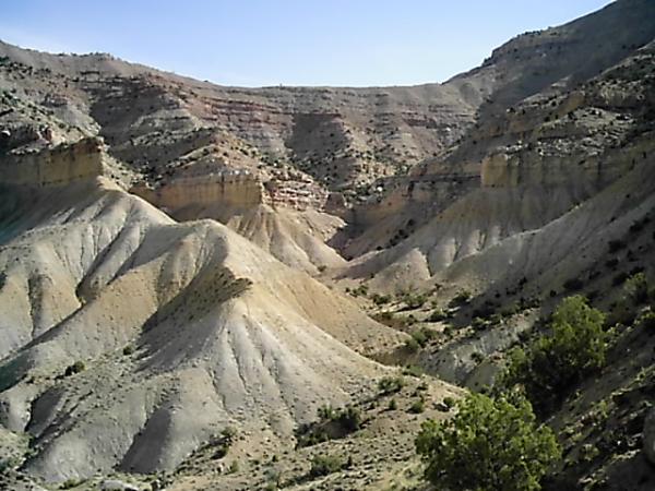 A scenic view of rugged, multicolored hills and canyons under a clear blue sky, showcasing layers of rock formations and sparse vegetation in a natural landscape. Zippety Do Dah mountain bike trail.