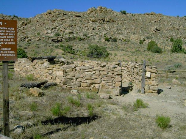 Remnants of a stone structure in a rocky, arid landscape, with signs of historical significance nearby. The site is surrounded by sparse vegetation and rocky terrain, indicating a remote and natural setting. Monitor &amp; Merrimac/Courthouse Pasture mountain bike trail.