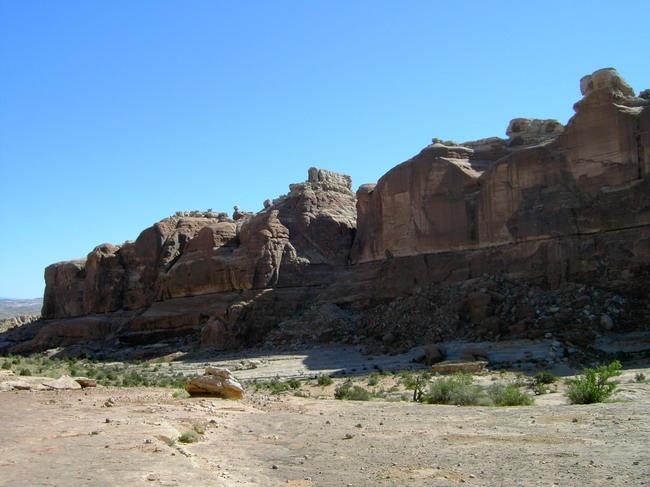 Rocky desert landscape featuring towering rock formations under a clear blue sky, with sparse vegetation in the foreground. Monitor &amp; Merrimac/Courthouse Pasture mountain bike trail.