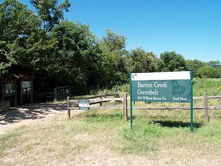 Sign for Barton Creek Greenbelt marking the trailhead, with a small information kiosk and surrounding greenery. Barton Creek Greenbelt mountain bike trail.