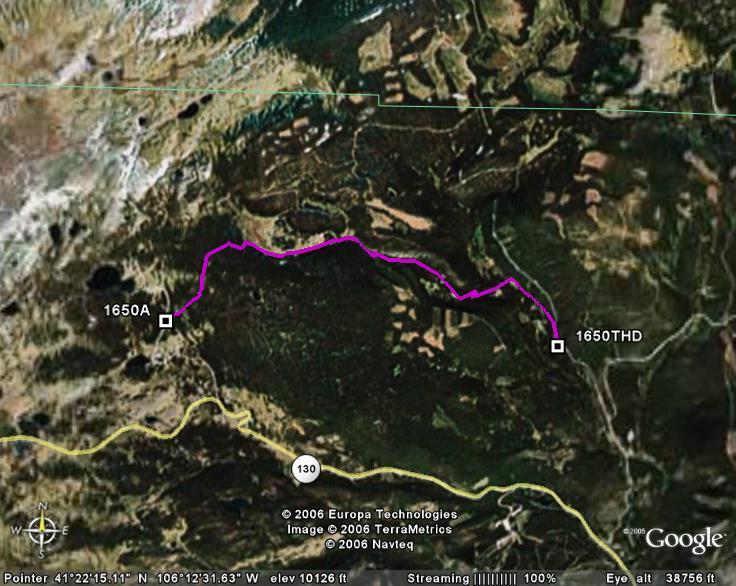 A satellite image showing a mountainous terrain with two marked locations labeled "1650A" and "1650THD." A pink line connects these points, indicating a path or route, while a yellow line runs horizontally across the bottom. The surrounding area features a mix of natural landscapes, including forests and patches of land, captured at a high elevation. North Fork Trail mountain bike trail.