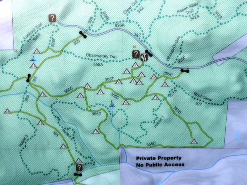 A detailed topographic map displaying various hiking trails, marked points of interest, and camping areas, along with indications of private property and restricted access. Key features include the Observatory Trail and surrounding paths, symbolized by green lines, along with icons representing campsites and landmarks. West Magnolia mountain bike trail.