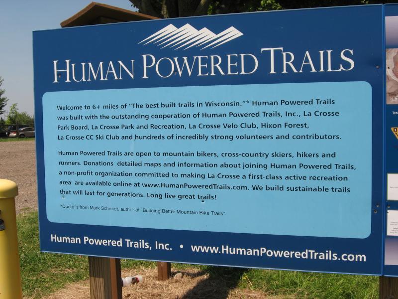 Signage for Human Powered Trails in Wisconsin, highlighting over 6 miles of well-built trails for mountain bikers, cross-country skiers, hikers, and runners. The sign includes information about the organization, its partners, and the dedication of volunteers. It invites donations and provides resources for joining the initiative, emphasizing the commitment to sustainable trail building. Hixon Forest mountain bike trail.