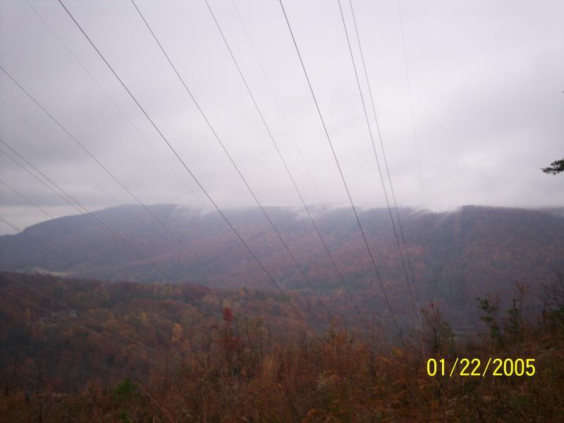 A scenic view of a mountainous landscape under a cloudy sky, featuring autumn foliage in shades of orange and brown. Power lines extend across the foreground, connecting to the distant hills that fade into the mist. The date in the corner reads January 22, 2005. Raccoon Mountain Trail Network mountain bike trail.