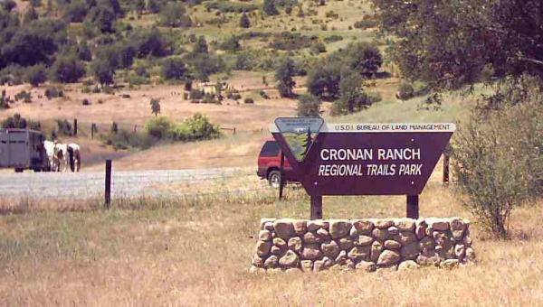 Sign for Cronan Ranch Regional Trails Park, with a dirt road and a red vehicle in the background, surrounded by grassy hills and trees. Up Down Trail mountain bike trail.