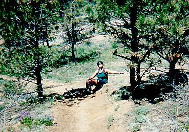 A person sitting on a dirt trail surrounded by trees in a natural outdoor setting, enjoying a sunny day. Chair Rocks mountain bike trail.