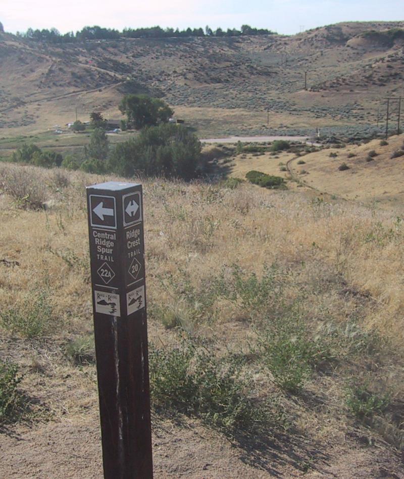 Trail signpost indicating the directions for the Central Ridge Spur Trail and the Ridge Crest Trail, with a hilly, grassy landscape in the background. Shane's Loop mountain bike trail.