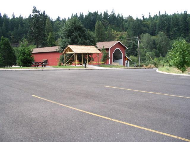 A view of a parking lot in front of a red building with a wooden canopy, surrounded by green trees and hills. The area appears quiet and is set in a natural landscape. Alpine Trail mountain bike trail.
