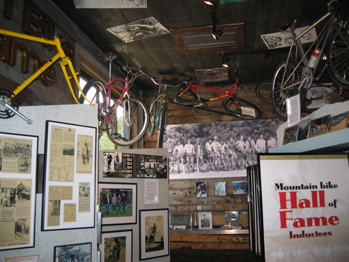 Interior view of a mountain bike hall of fame exhibit featuring bicycles mounted on the walls, historical photographs, and informational panels detailing inductees and the history of mountain biking.