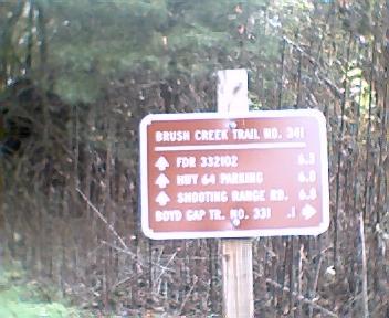 A brown trail sign indicating directions and distances for various routes including Brush Creek Trail No. 341, FDR 332102, Highway 64 Parking, Shooting Range Road, and Boyd Gap Trail No. 331, set against a backdrop of trees. Brush Creek mountain bike trail.