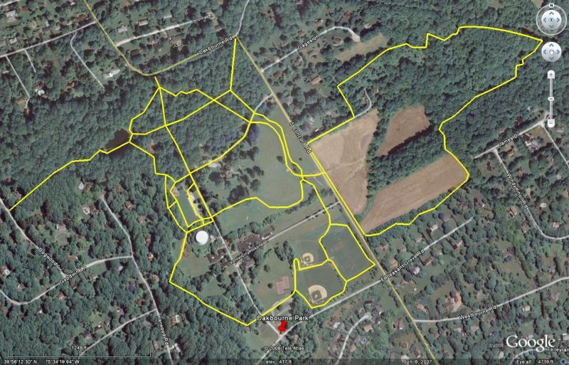 Aerial view of Oakbourne Park and surrounding areas, featuring outlined trails and paths in yellow against a backdrop of wooded areas, fields, and residential streets. The image highlights park facilities, including baseball fields and open green spaces. Oakbourne Park mountain bike trail.