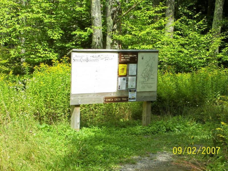 A wooden information sign for the Seneca Creek Trail located in a forested area. The sign features a blank space for visitor information, several bulletins and maps attached to it, and is surrounded by green foliage and trees. The date at the bottom of the image indicates September 2, 2007. Spruce Knob Loop mountain bike trail.