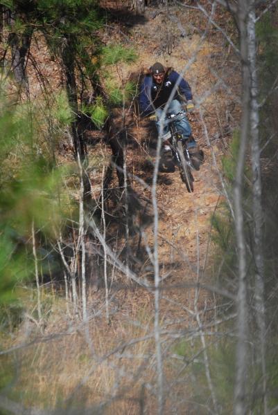 A mountain biker navigating a steep, dirt trail surrounded by trees, demonstrating balance and skill while riding downhill. The Clay Pits mountain bike trail.