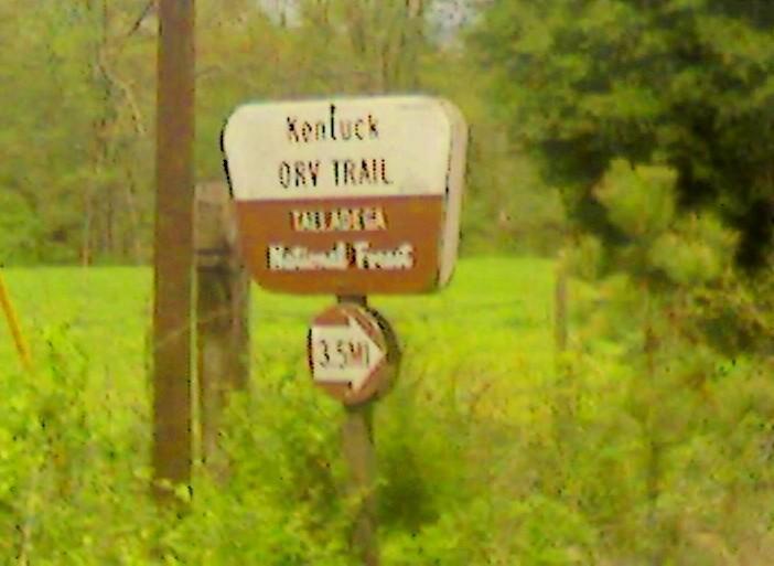 Sign marking the Kentucky Dry Trail, indicating a distance of 3.5 miles and stating it is part of the National Forest. Surrounding greenery includes trees and open fields. Kentucky Orv mountain bike trail.
