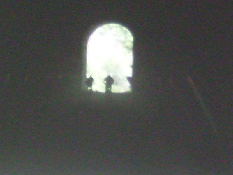 Silhouettes of two figures standing in front of an arched window, illuminated by soft, natural light coming from outside. The surrounding area is dark, creating a contrast between the brightness of the window and the shadows in the foreground. Bizz Johnson Trail mountain bike trail.