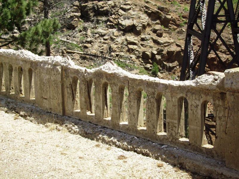 A weathered stone wall with arched openings, overlooking a rocky landscape. Lush greenery is visible in the background, indicating a natural setting. The wall shows signs of aging and erosion, adding to its rustic charm. Bizz Johnson Trail mountain bike trail.