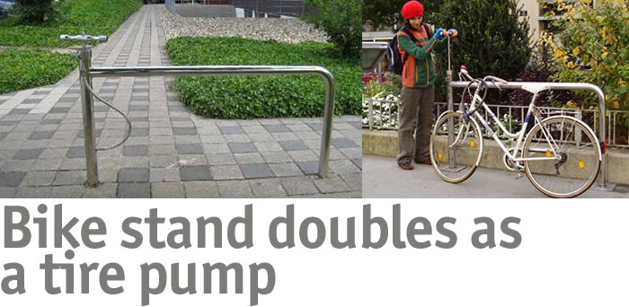 Image showing a unique bike stand that also functions as a tire pump. On the left, the bike stand is anchored in the ground, while on the right, a person in a red hat is using the stand to inflate a bicycle tire. The background features greenery and a pedestrian walkway.