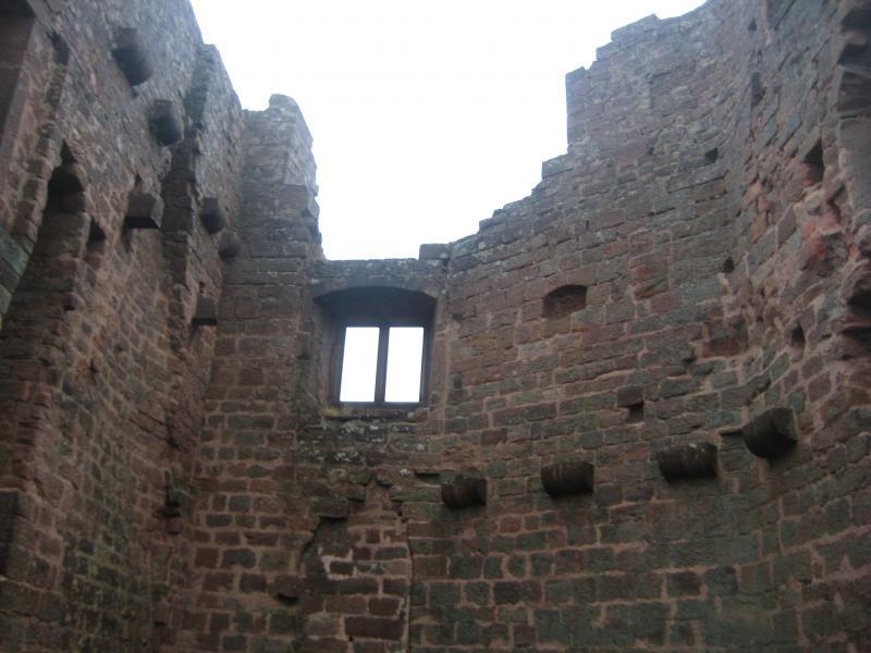 Ruins of an old stone structure, viewed from inside looking up towards a window, with exposed brick walls and sections of stone remaining visible against a cloudy sky. Hohenecken Trails mountain bike trail.