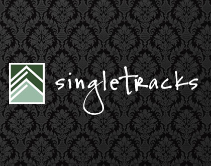 Logo of Singletracks featuring a green and white icon of stylized trees or mountains alongside the word "singletracks" in a casual handwritten font, set against a textured black damask background.