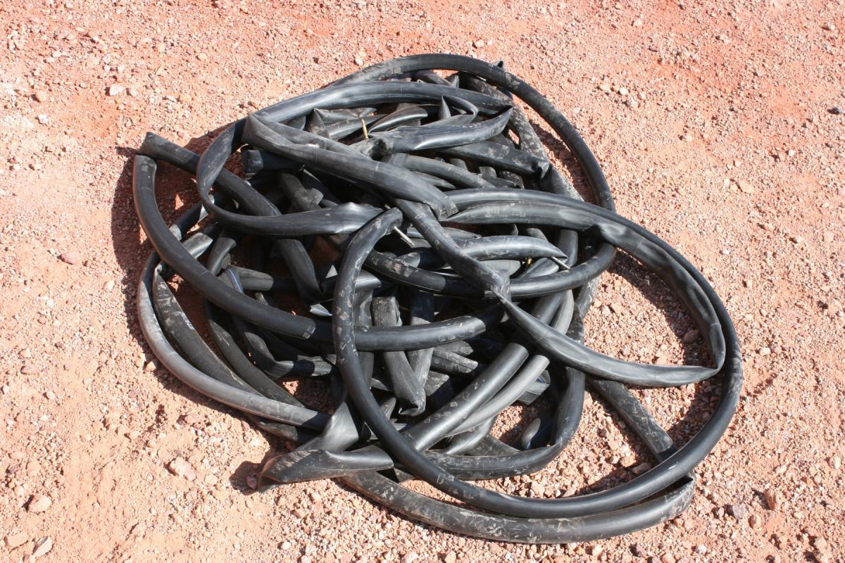 A pile of tangled black rubber tubes resting on a sandy surface. The tubes are coiled and overlapping, creating a chaotic appearance. Bootleg Canyon mountain bike trail.
