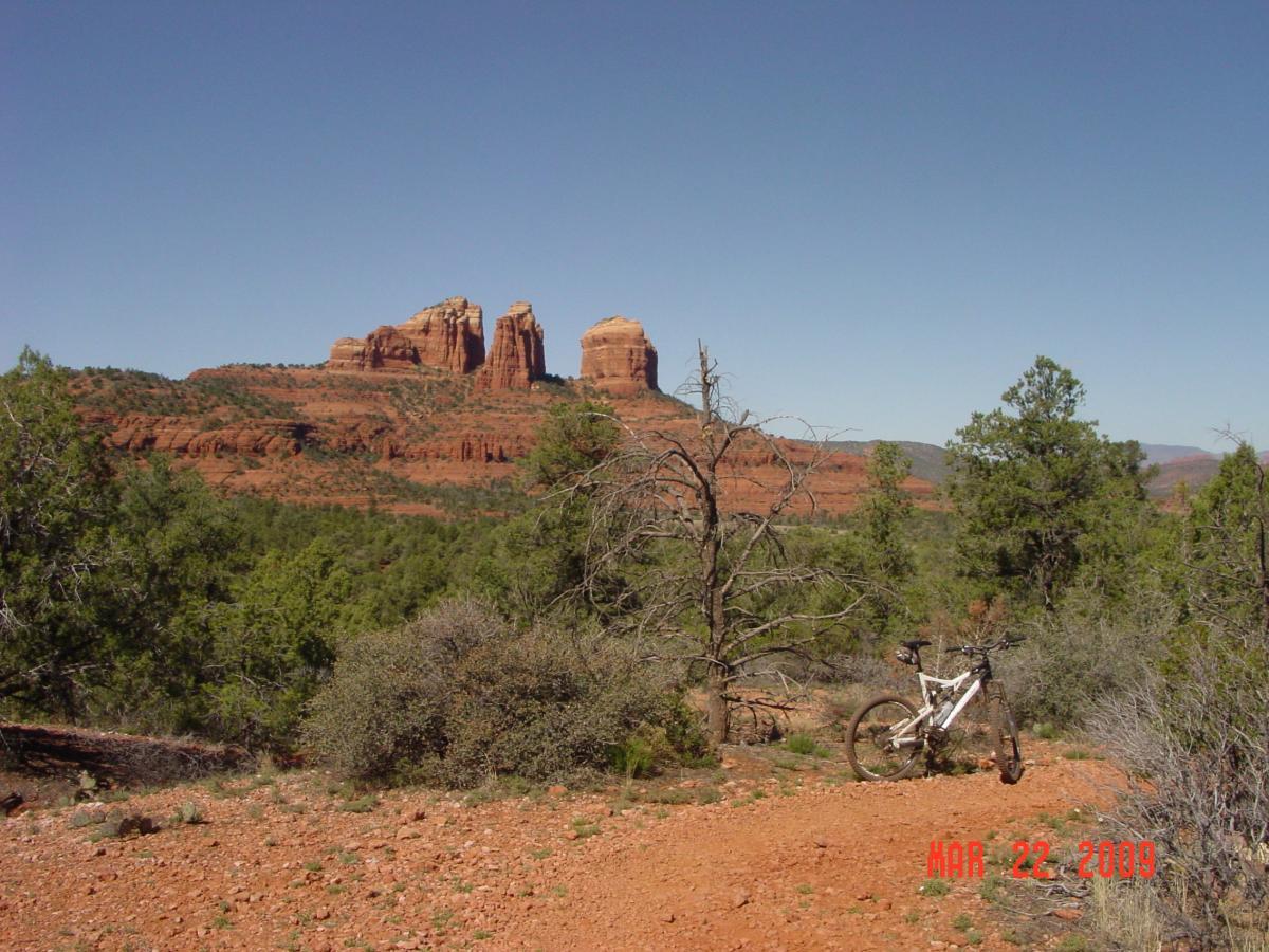 A mountain bike rests on a dirt path in a scenic landscape, with red rock formations and green vegetation in the background under a clear blue sky. The date "MAR 22, 2009" is visible in the lower right corner. Templeton mountain bike trail.
