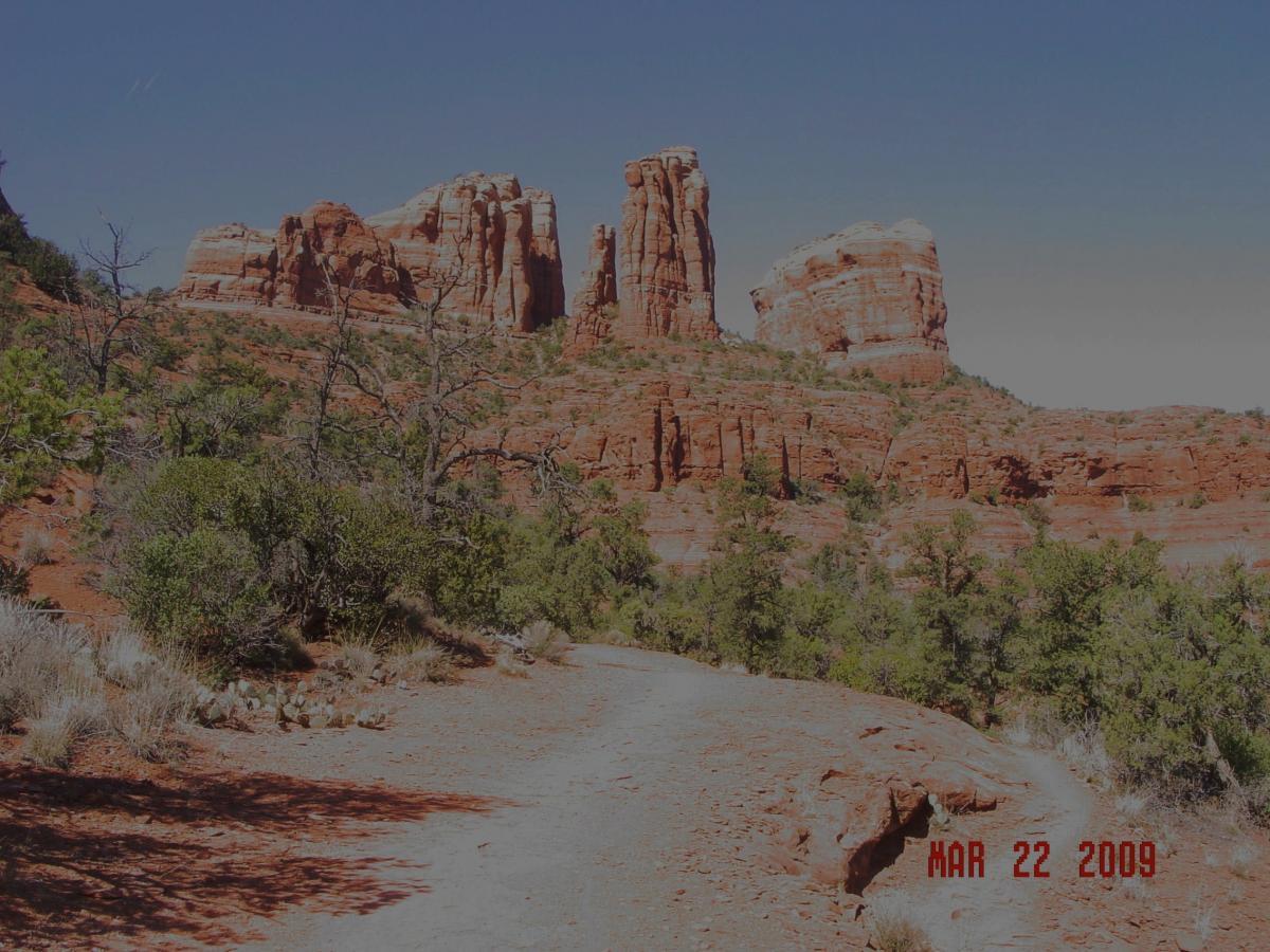 A scenic landscape featuring red rock formations and a desert trail surrounded by sparse vegetation, under a clear blue sky. The photo is dated March 22, 2009. Templeton mountain bike trail.